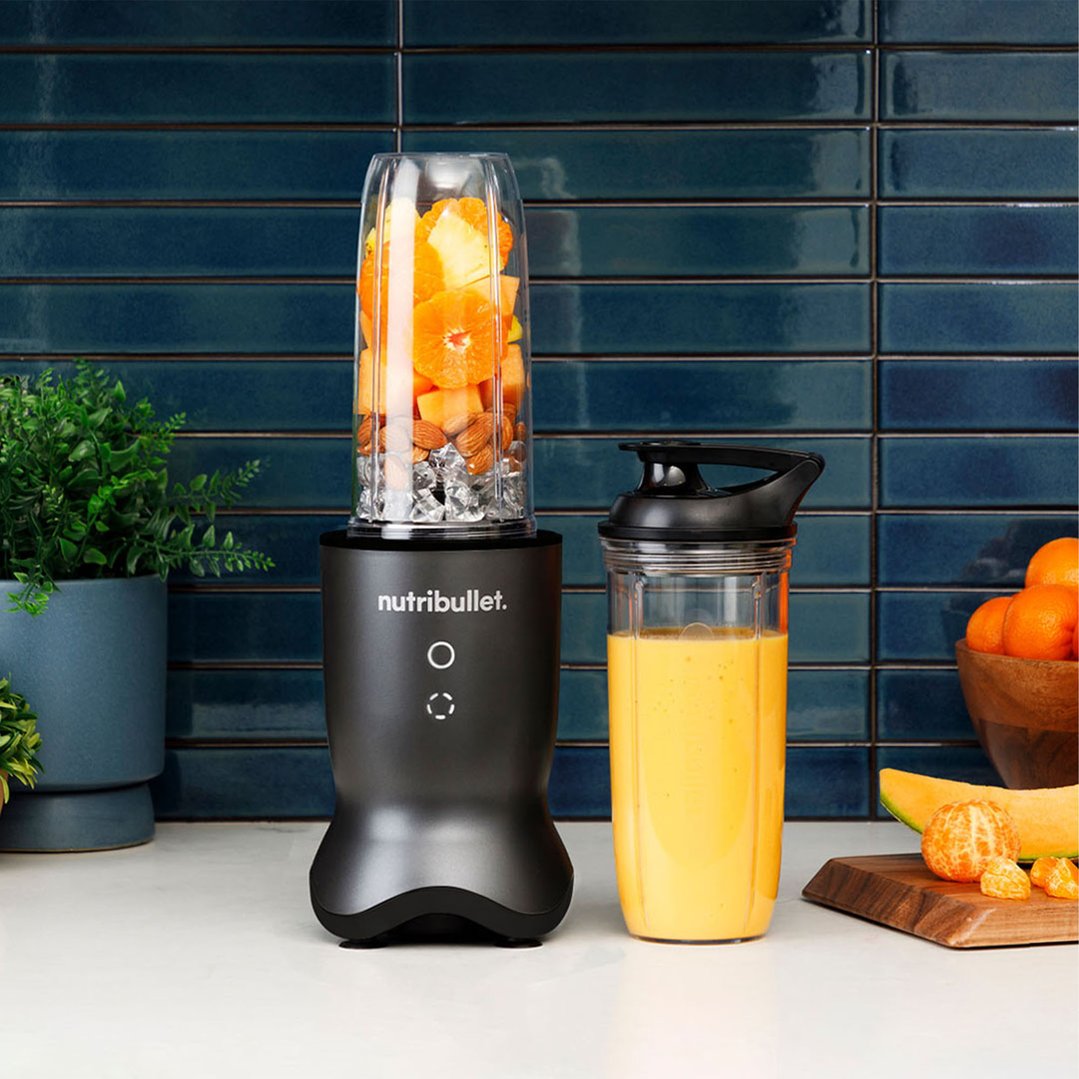 Black NUTRiBULLET blender with fruit and ice, next to a cup of smoothie