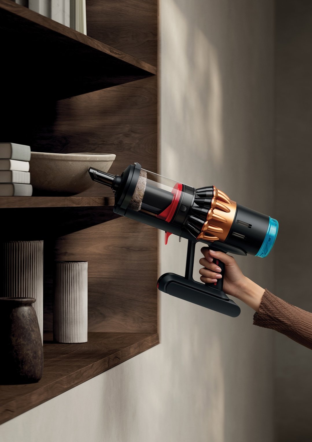 Hand holding a Dyson handstick vacuum, cleaning a wooden bookshelf