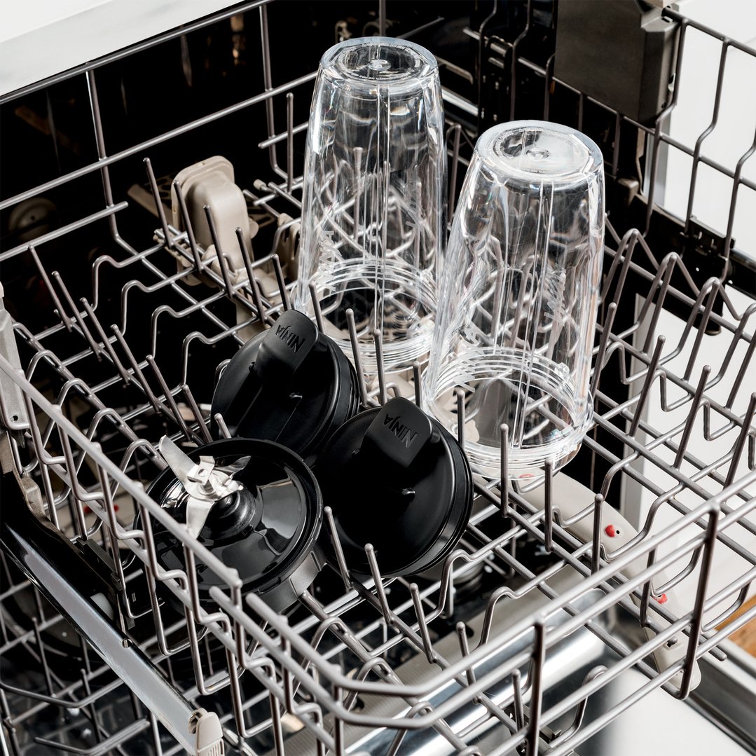 Ninja blender cups and lids in the bottom rack of a dishwasher