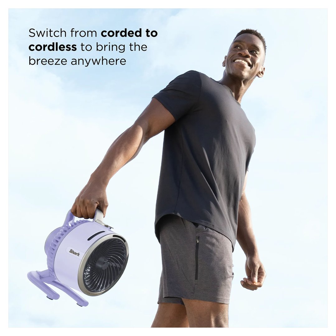 Man holding a lilac Shark portable fan outdoors under a blue sky
