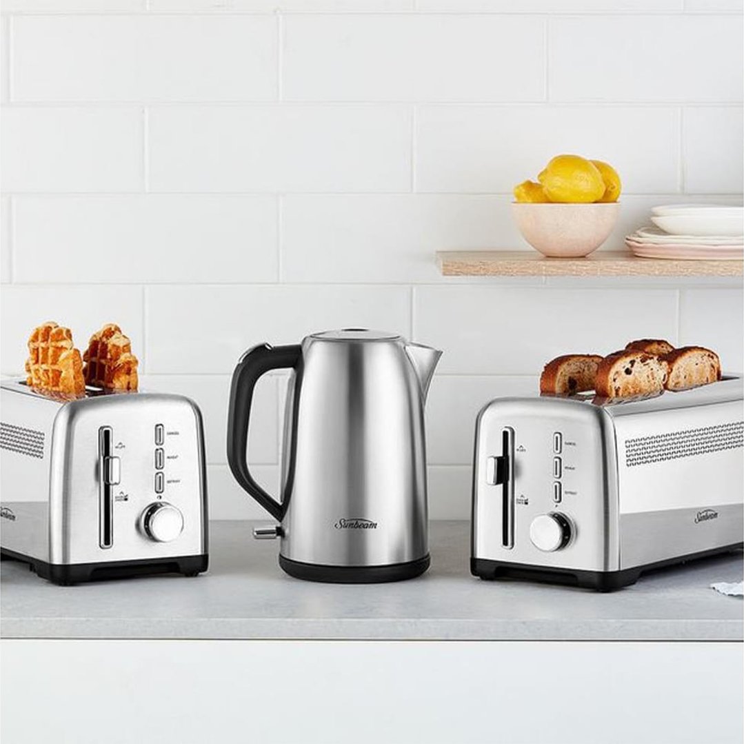 Stainless steel kettle and two toasters on a kitchen counter with white subway tiles