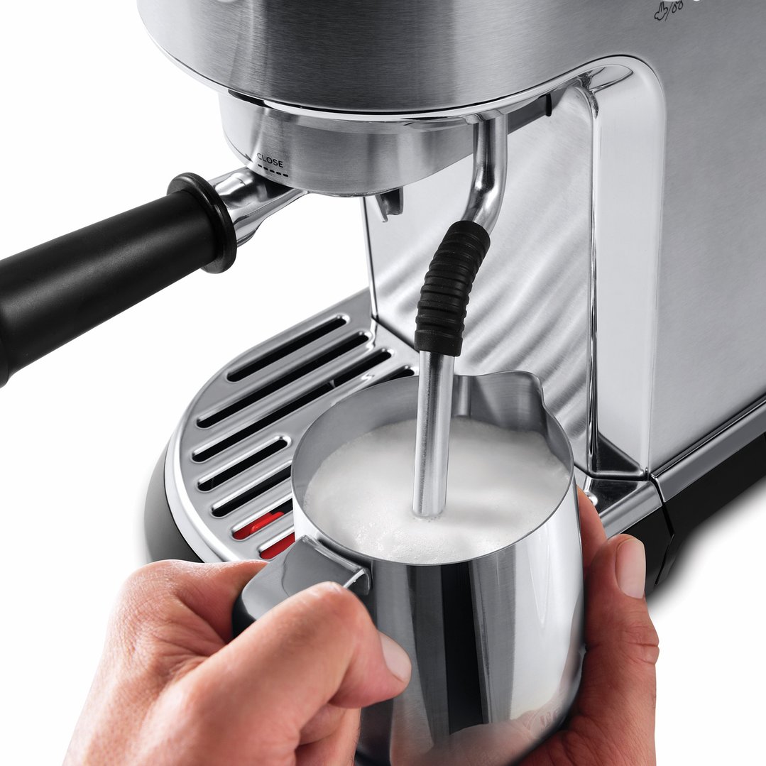 Hands holding a milk jug under the steam wand of a coffee machine