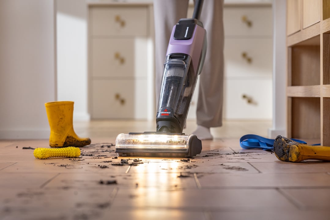 BISSELL handStickVacuum cleaning a muddy floor with a person standing in the background