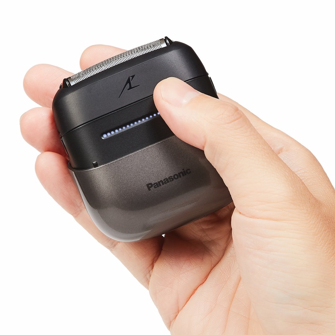 Hand holding a black Panasonic shaver with illuminated indicator lights