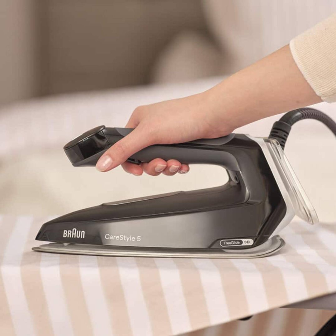 Hand holding a Braun CareStyle 5 steam generator iron on an ironing board