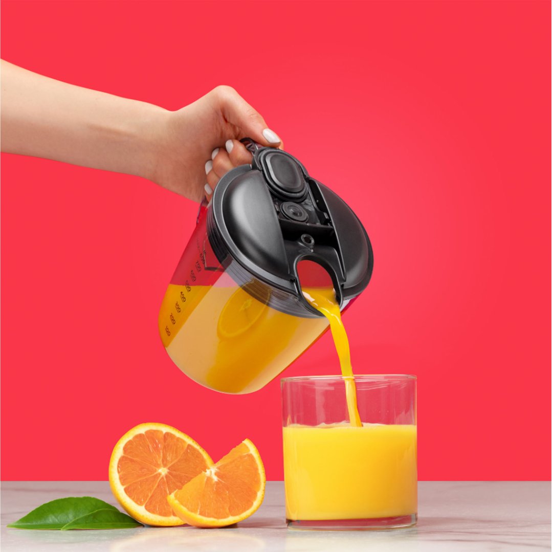 Hand pouring orange juice from a juicer into a glass with oranges nearby