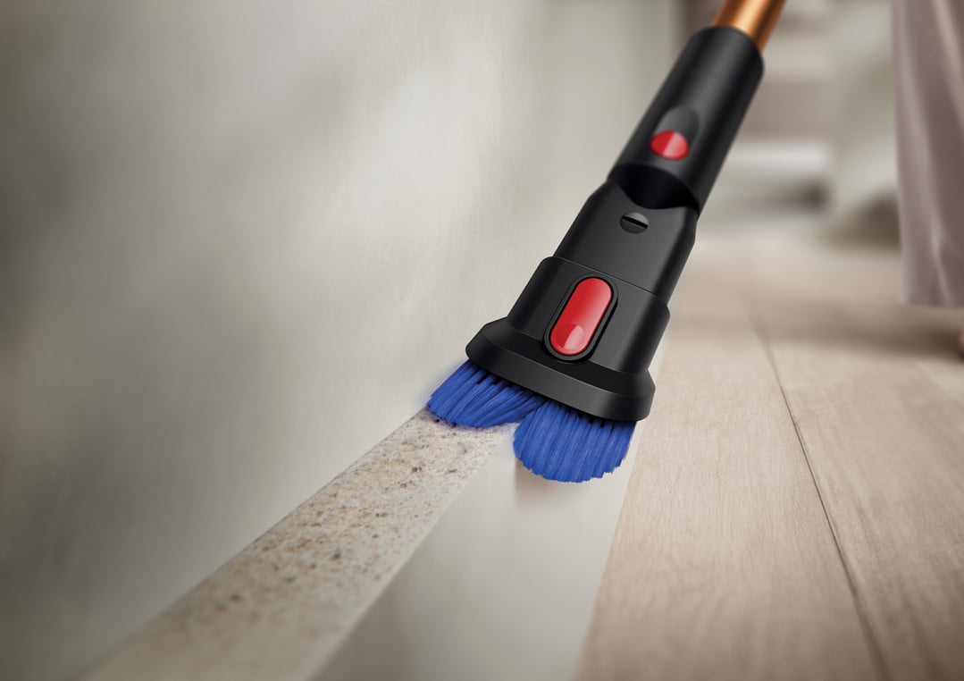 Dyson handstick vacuum cleaning dirt from a floor edge with a brush attachment