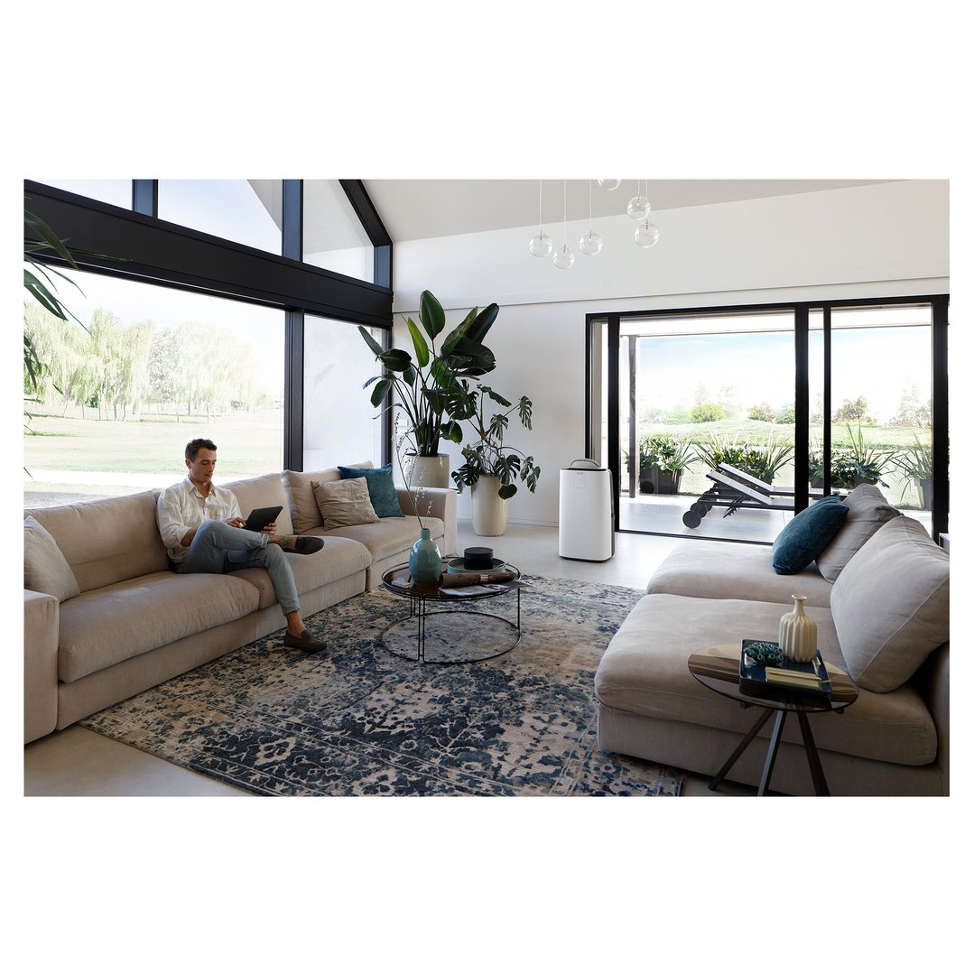 Man on a sofa using a tablet in a modern living room with an air conditioner