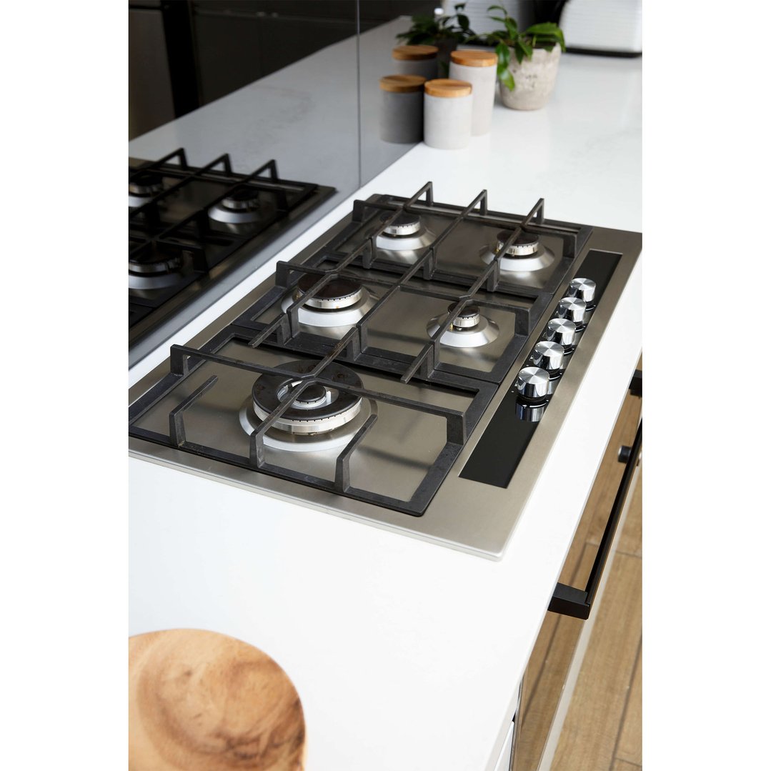 Stainless steel gas cooktop with five burners and control knobs on a white countertop