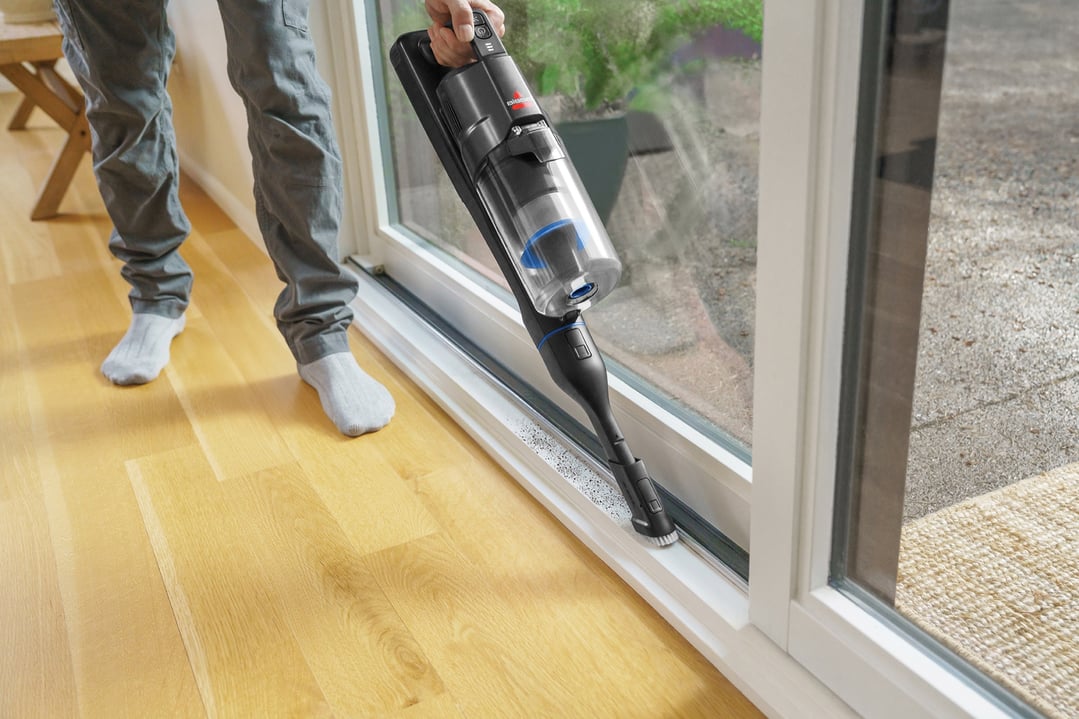 Person in socks using a BISSELL handStickVacuums to clean a sliding door track