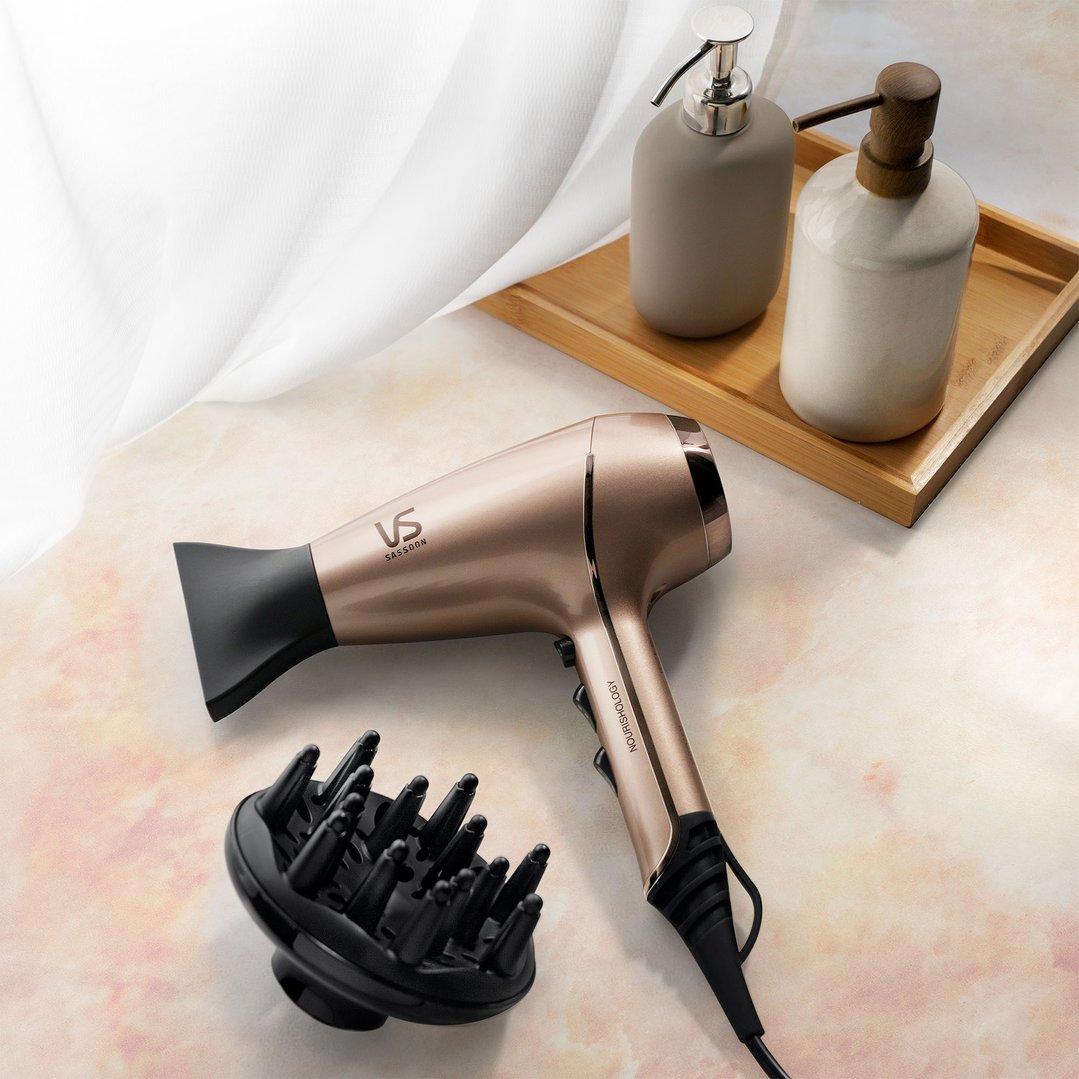 Rose gold hair dryer and diffuser on a marble surface with two soap dispensers