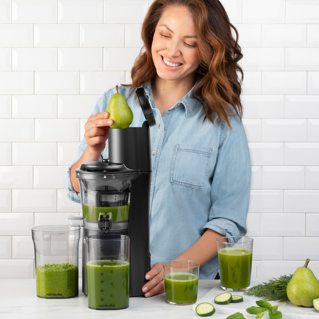 Woman using a NUTRiBULLET slow juicer to make green juice with a pear