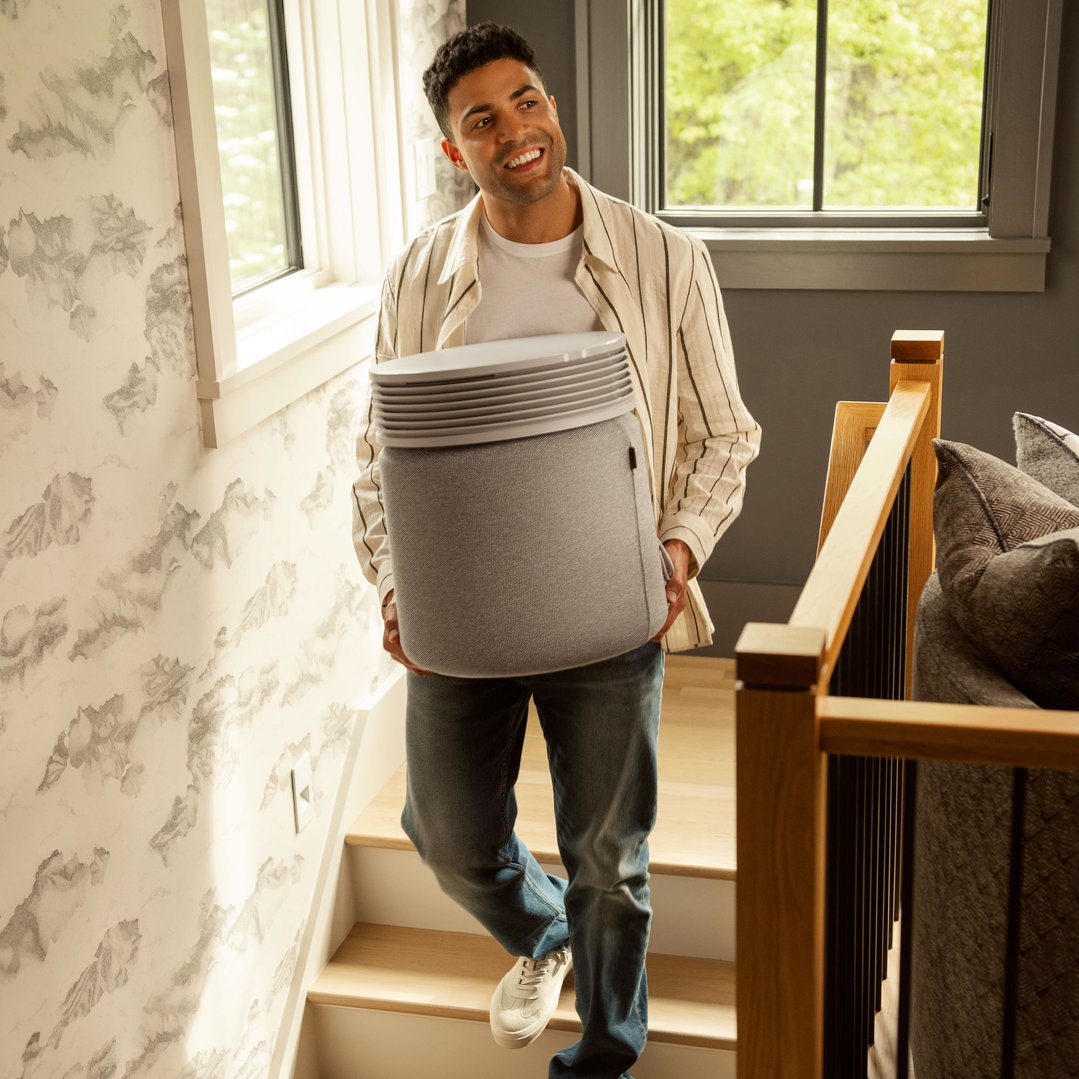 Man carrying a light grey Blueair air purifier up a wooden staircase