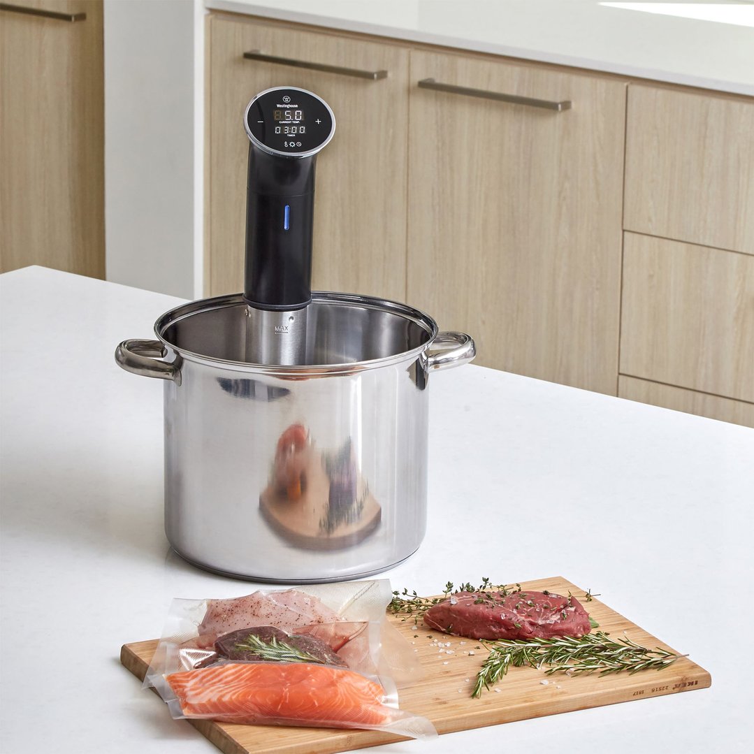 Sous vide immersion cooker in a pot with vacuum-sealed food on a cutting board