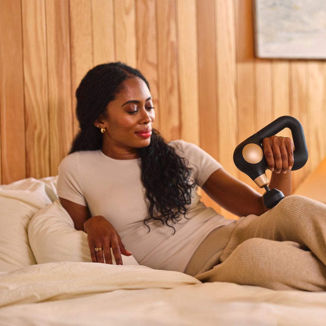 Woman lying on a bed using a black and gold massager on her arm