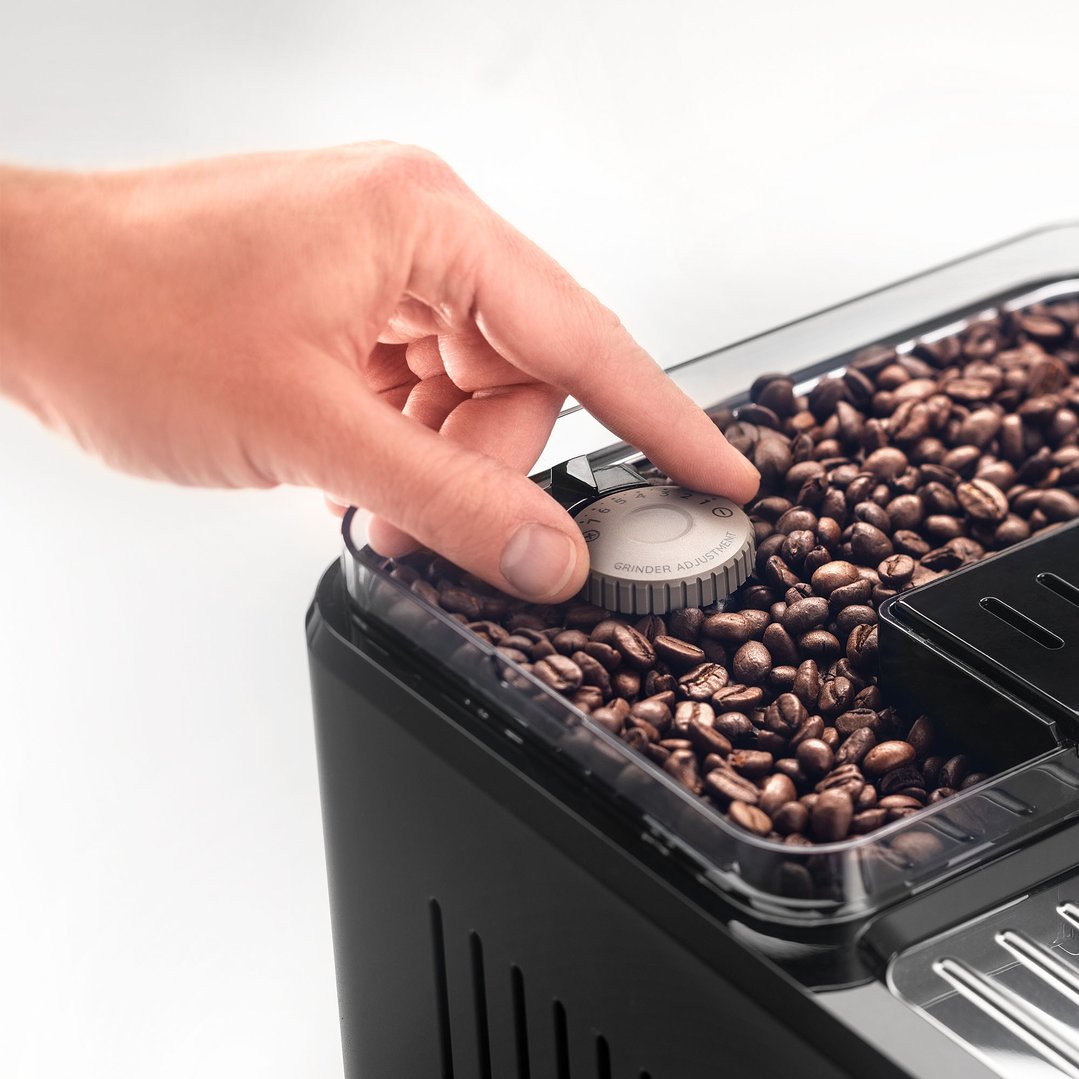 Hand adjusting the grinder setting on a coffee machine filled with coffee beans