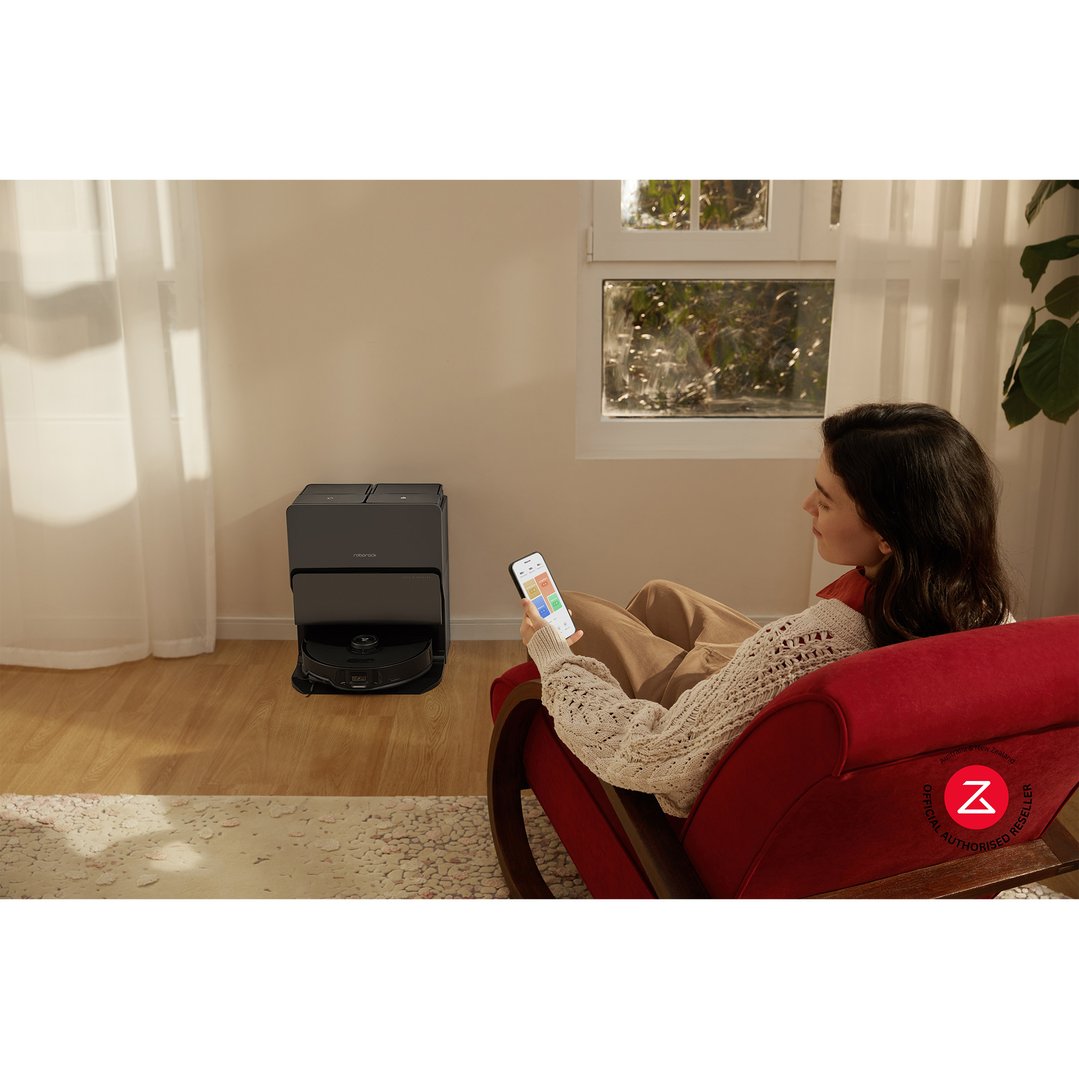 Woman sitting on a red armchair, using a smartphone to control the robotic vacuum