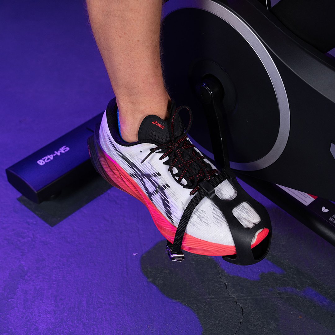 Person's foot in a white and pink shoe on a spin bike pedal