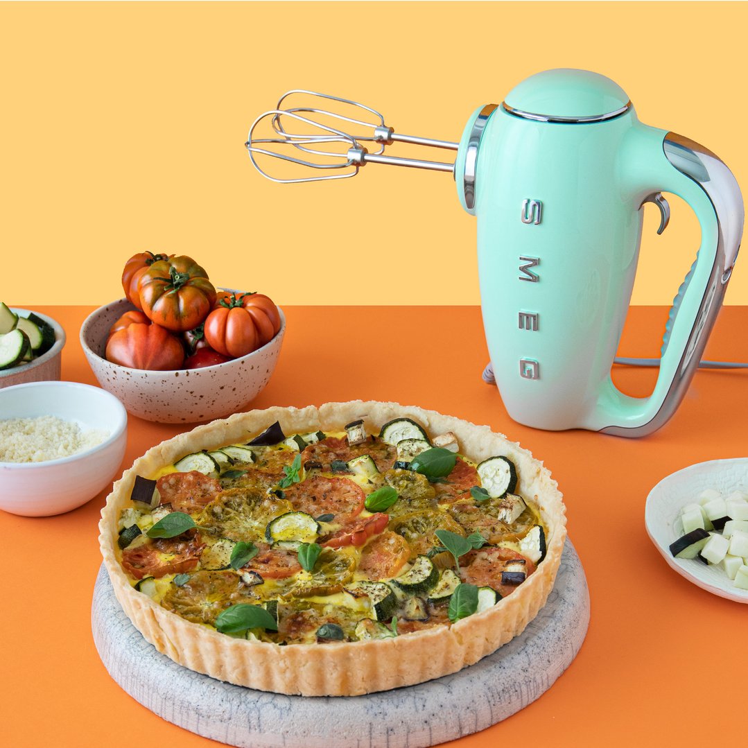 Green Smeg hand mixer and a vegetable tart on an orange surface