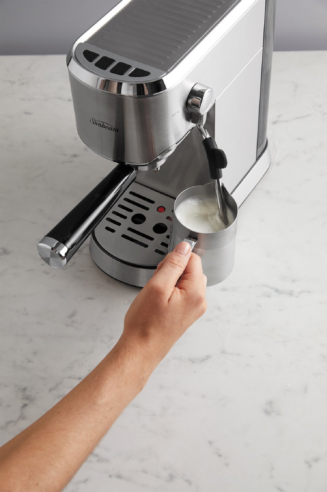 Hand frothing milk with the Sunbeam Compact Barista Espresso Machine on a marble counter
