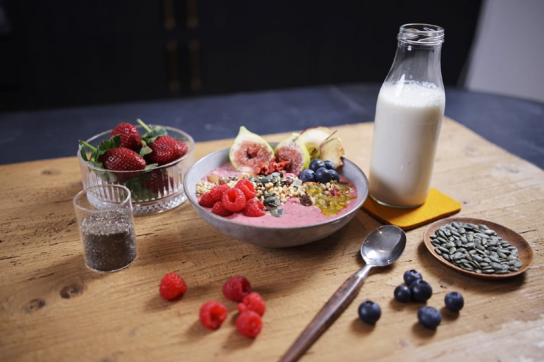 A smoothie bowl with fruits and seeds, milk, and chia seeds on a wooden table