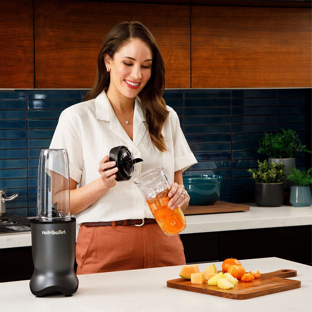 Woman preparing a NUTRiBULLET blender with fruit and liquid in a kitchen setting