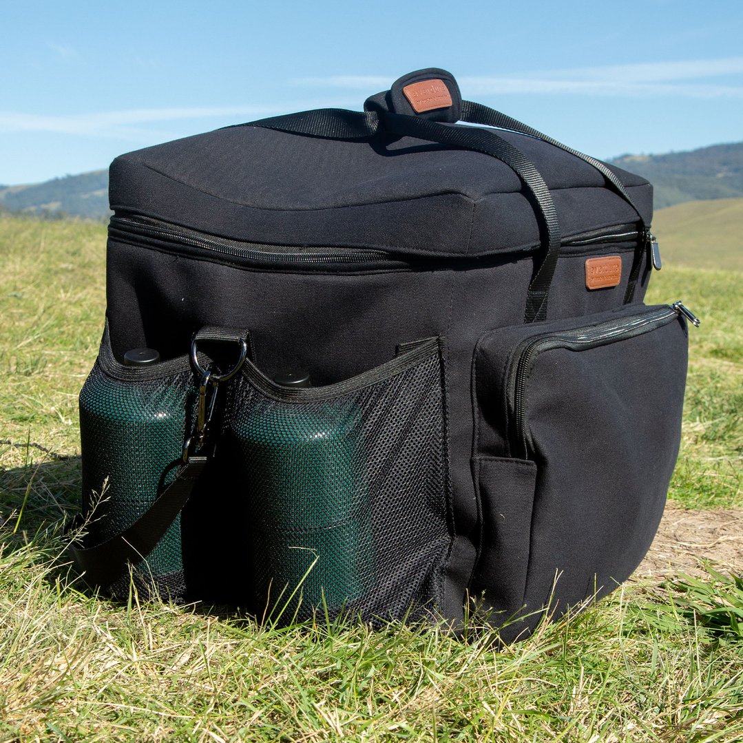Black carrier bag with two green bottles in mesh pockets on grass outdoors