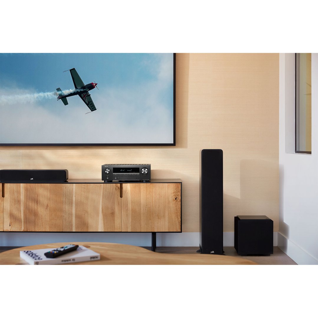 AV receiver and speakers on a wooden cabinet below a TV showing an airplane