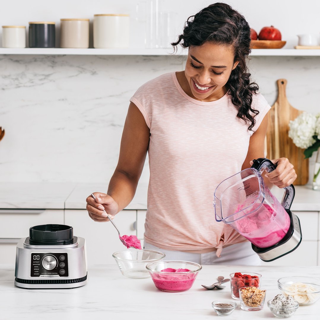 Woman serving pink smoothie from a Ninja blender into bowls