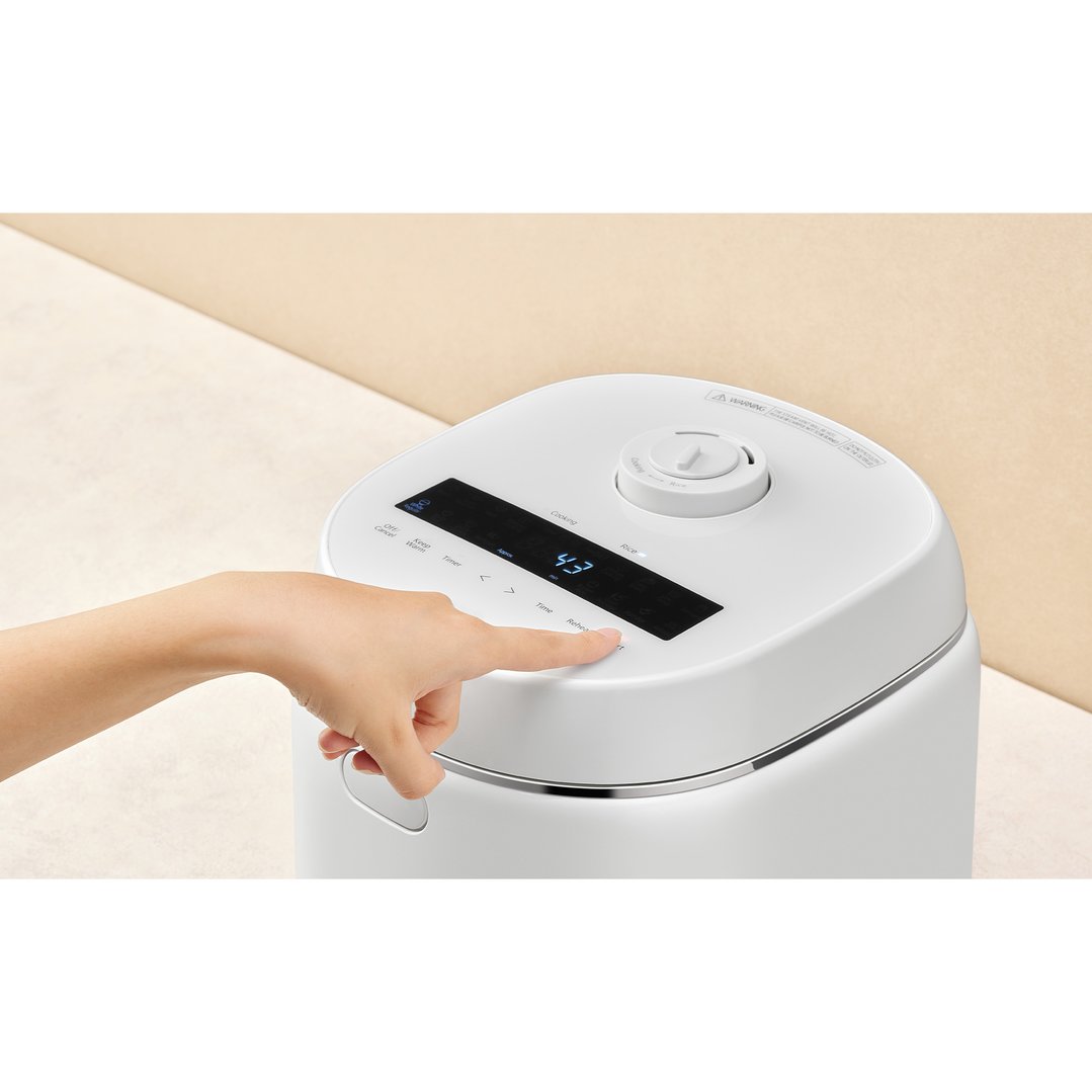 Hand pressing a button on the control panel of a white rice cooker