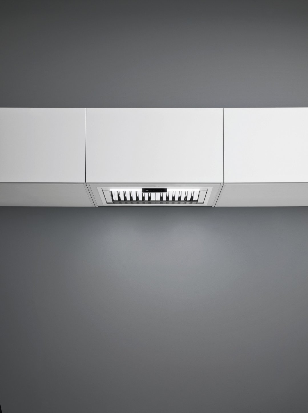Undermount rangehood integrated into white kitchen cabinetry with dark grey wall