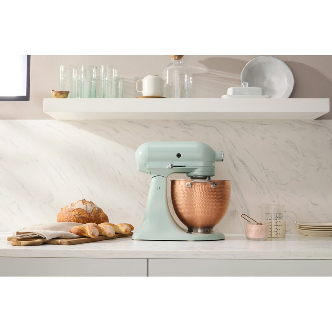 A light green stand mixer with a copper bowl on a kitchen counter with bread