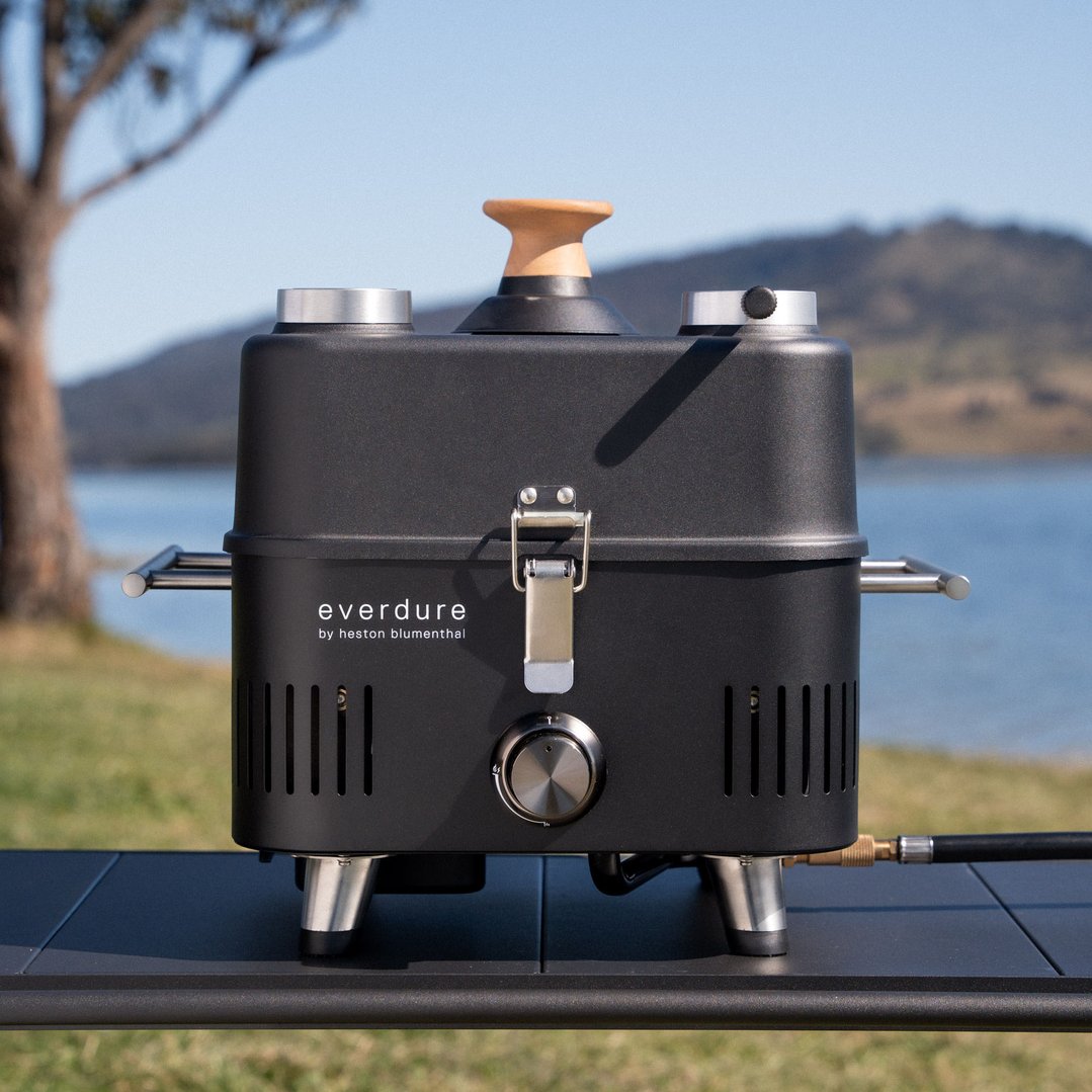 Black portable BBQ on a table outdoors with a lake and mountains in the background