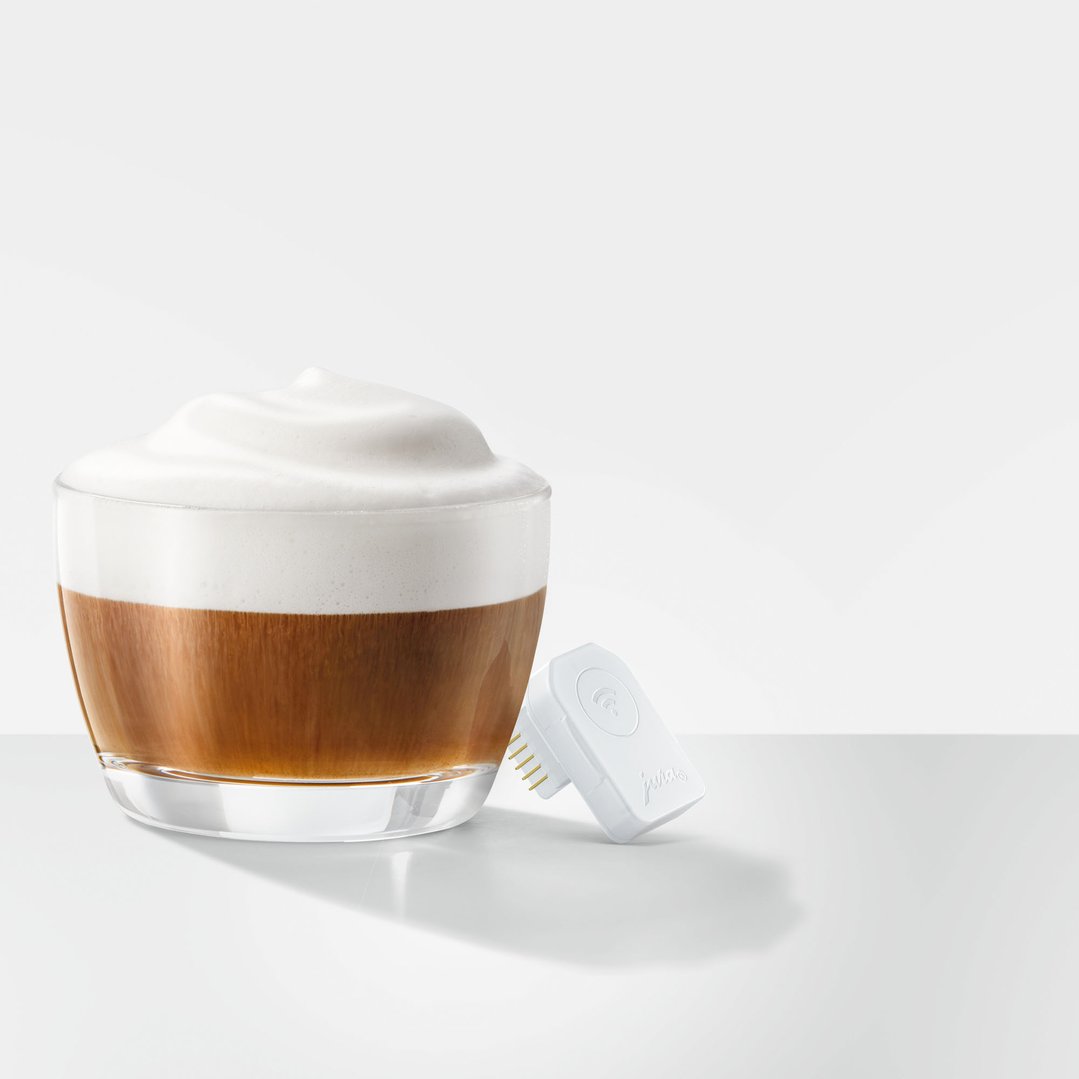 JURA Wi-Fi Connect V2 next to a glass of latte on a white surface