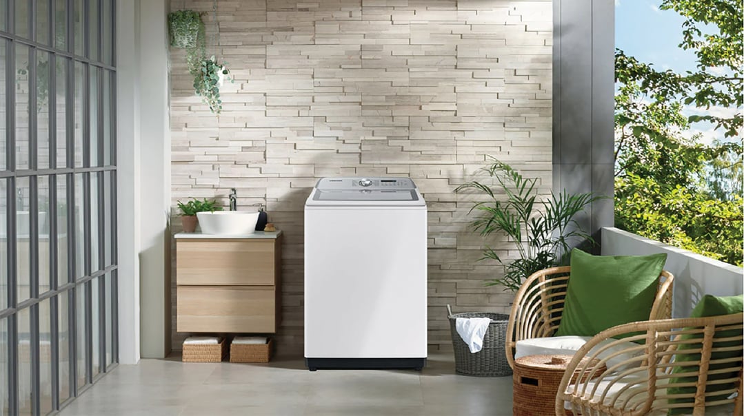 White top load washing machine on a balcony with plants and wicker chairs