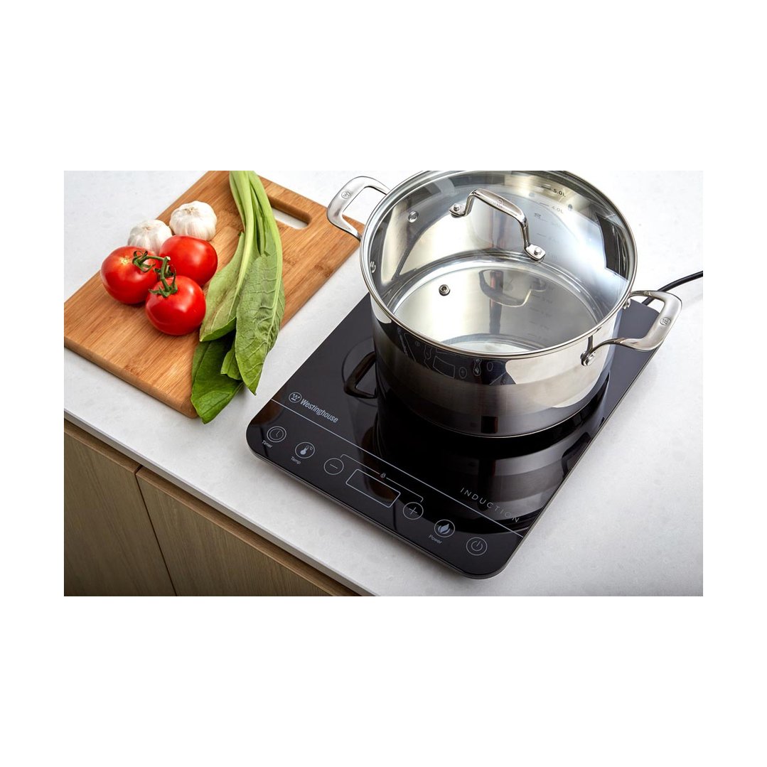 Induction cooktop with a pot on it, next to a cutting board with vegetables