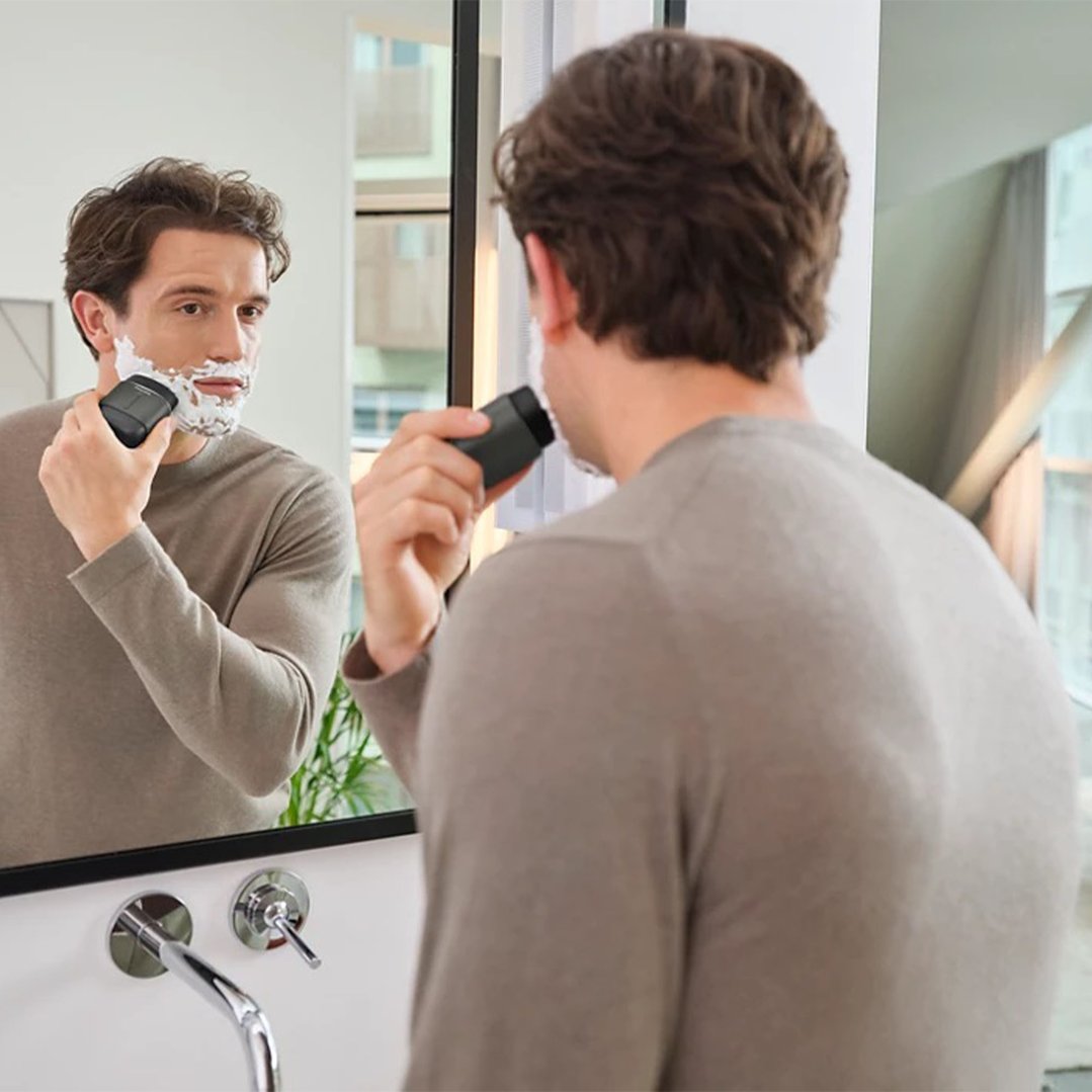 Man shaving with a Philips electric shaver in front of a mirror
