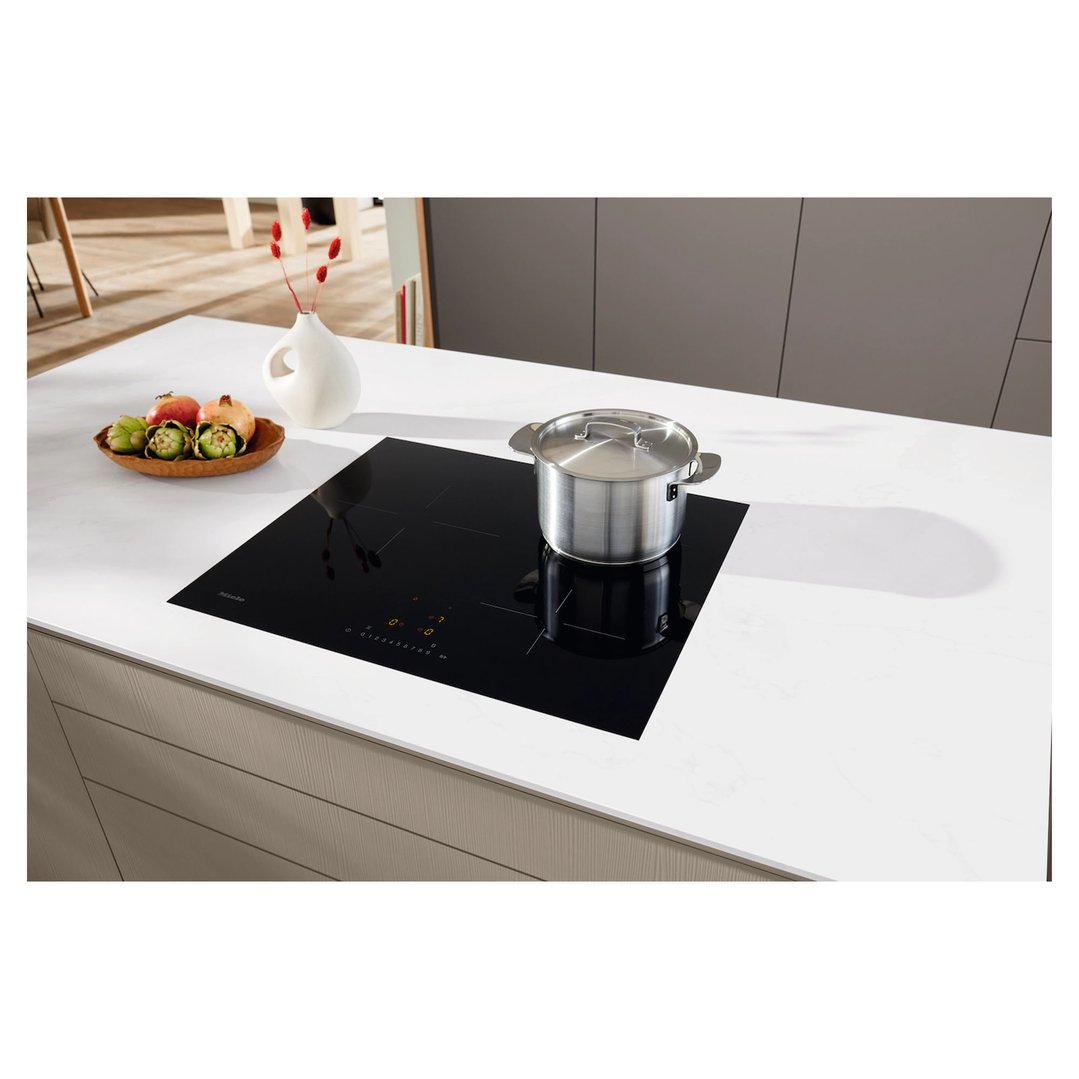 Black induction cooktop with a pot on a white kitchen counter with fruit