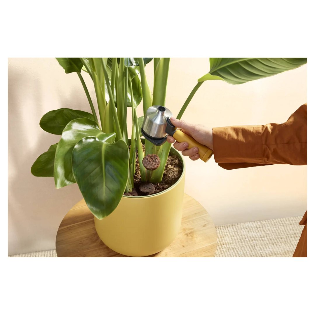 Hand using a portafilter to add coffee grounds to a potted plant