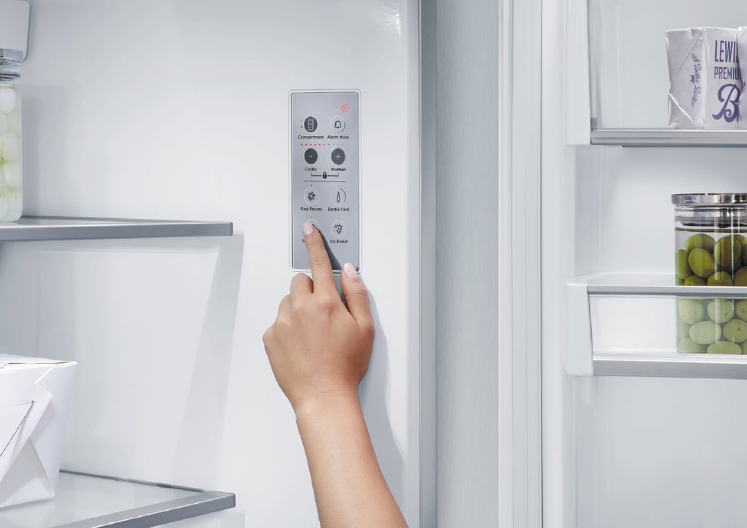 Hand pressing a button on the control panel of an open refrigerator freezer