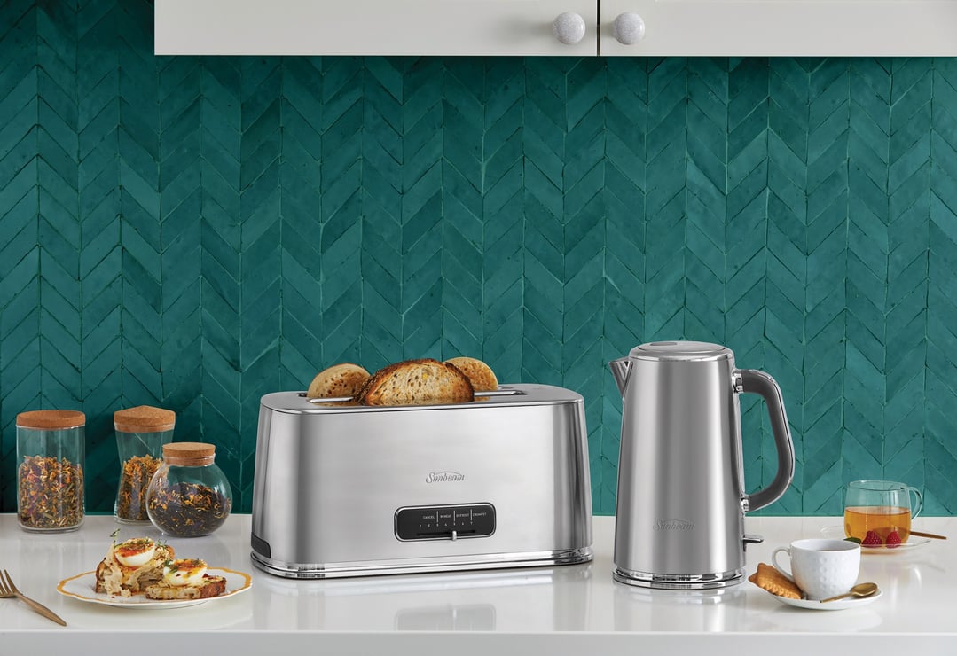 Stainless steel toaster and kettle on a white counter with teal tile backsplash