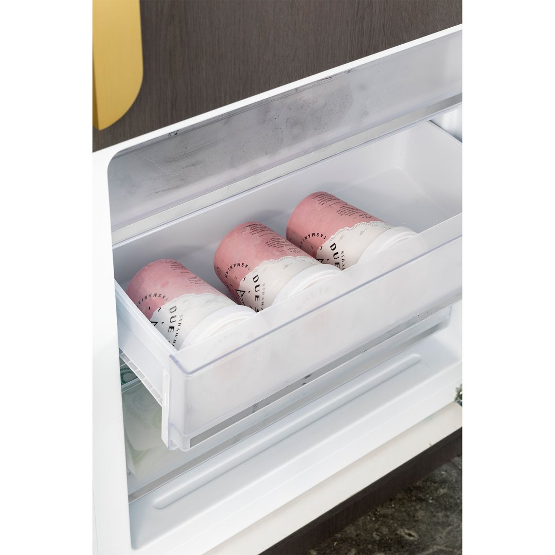 Three tubs of strawberry ice cream stored in the freezer drawer of a fridge