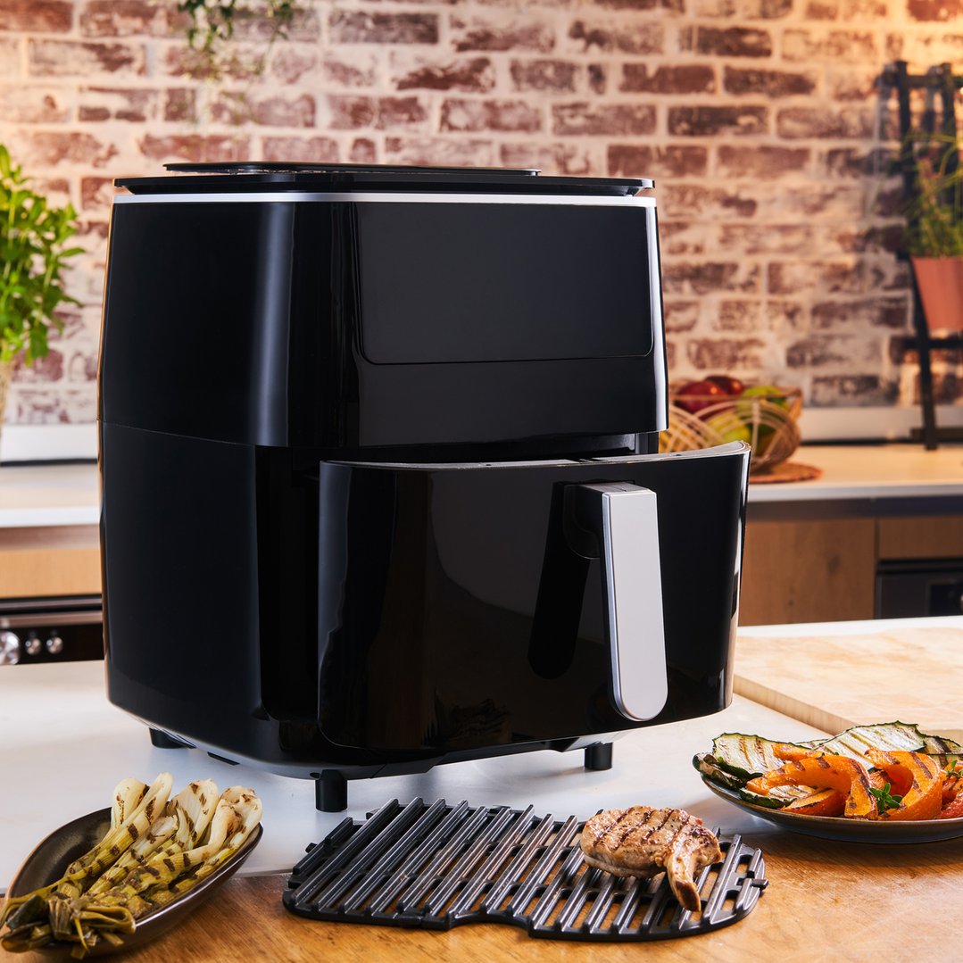 Black TEFAL air fryer on a kitchen counter with grilled food