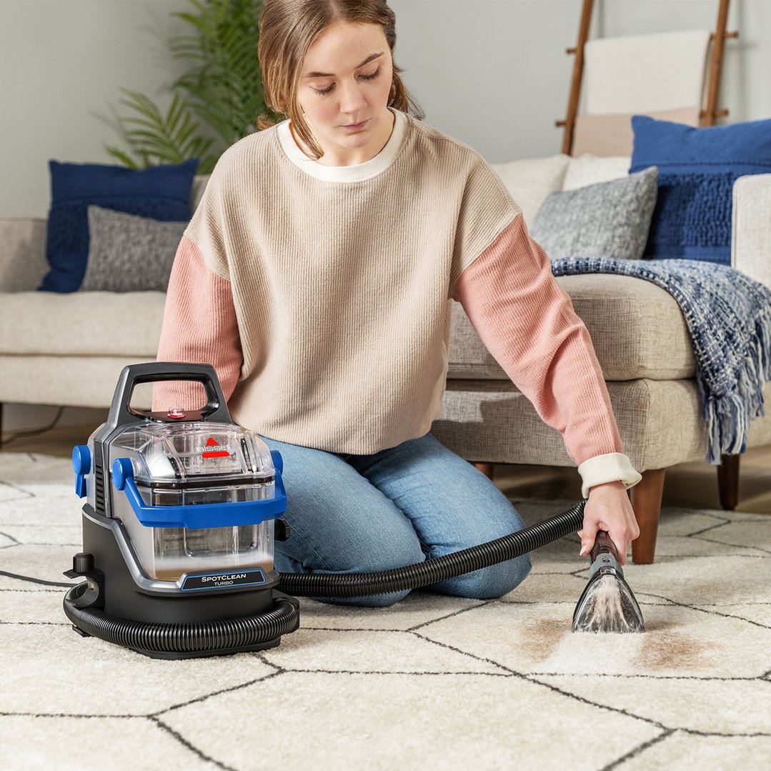 Woman kneeling on rug, cleaning a stain with a BISSELL SpotClean Turbo vacuum cleaner