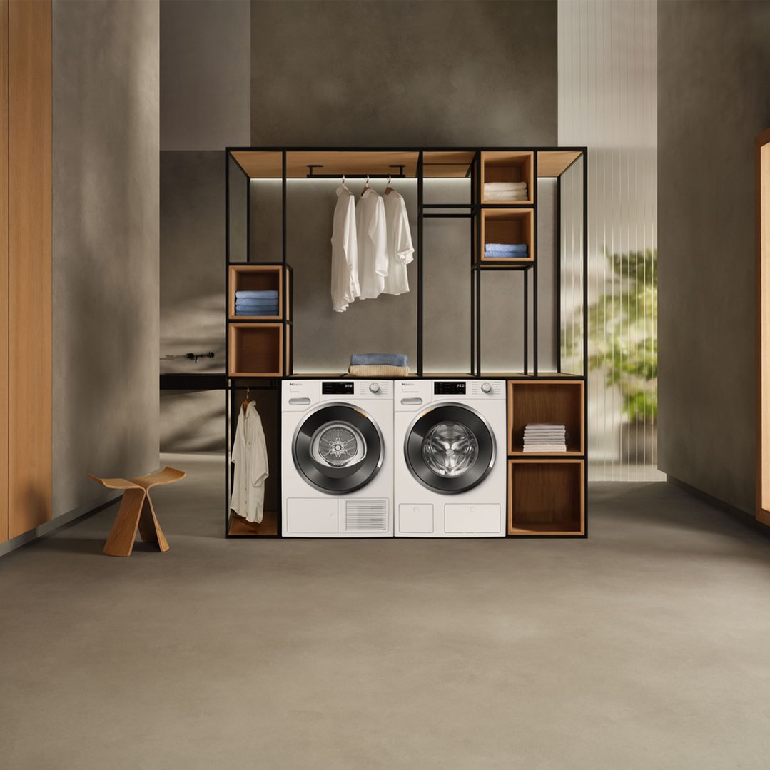 Two washing machines in a modern laundry room with wooden shelving and clothes