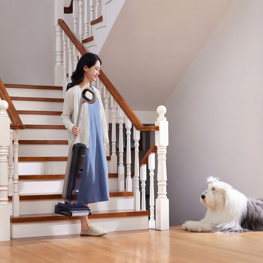 Woman holding a TINECO vacuum cleaner on stairs with a dog nearby