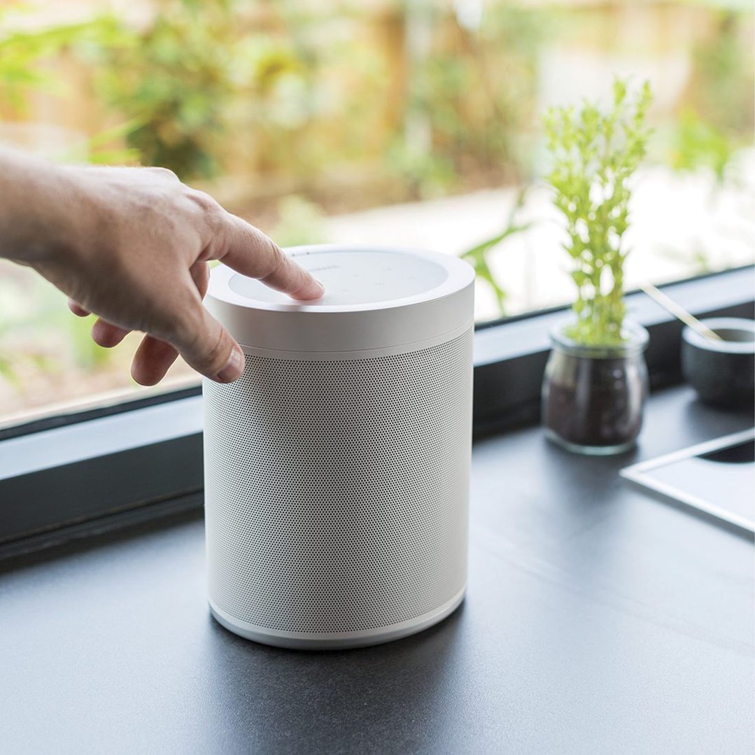 Hand pressing the top controls of a white Yamaha MusicCast 20 wireless speaker