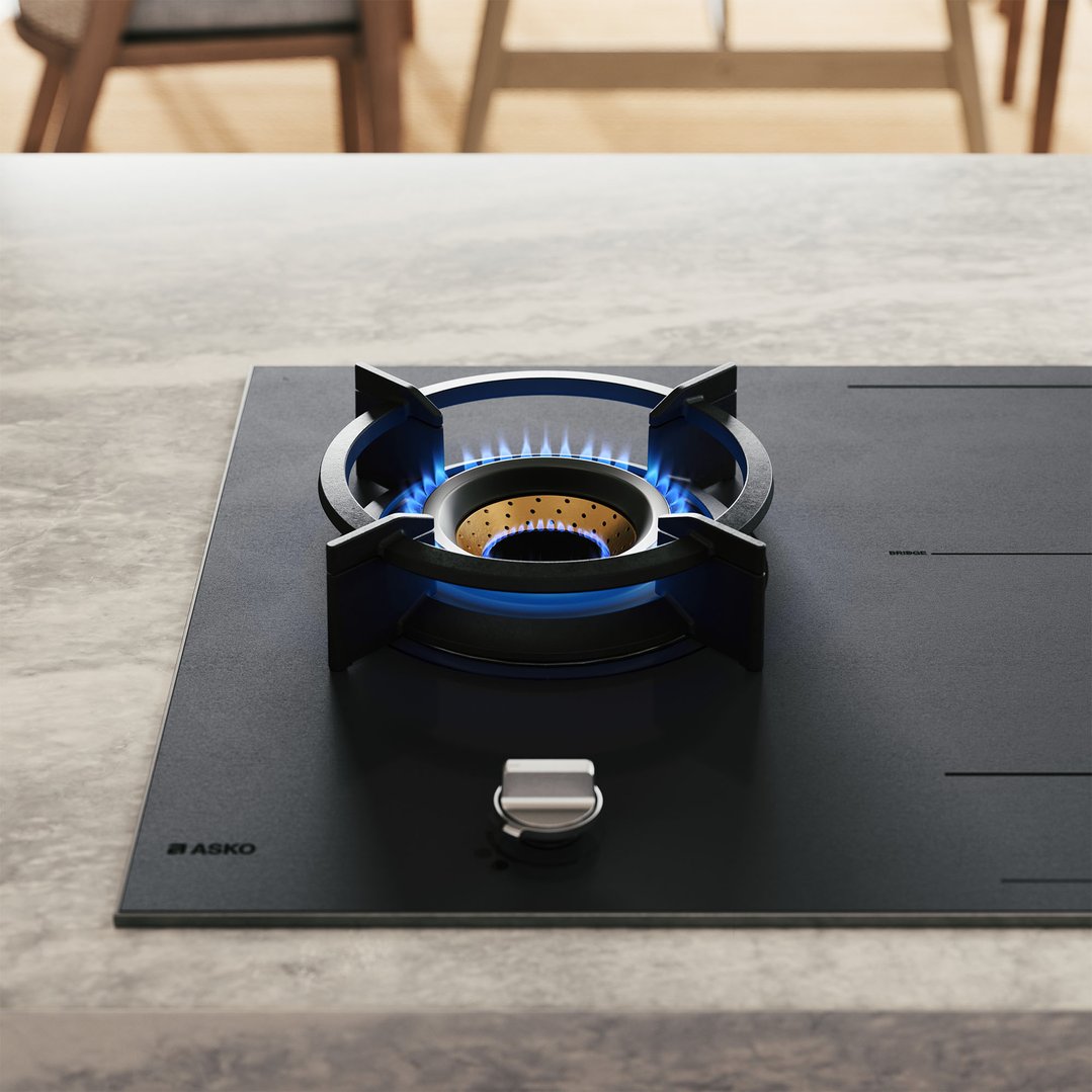 Close up of a gas cooktop burner with blue flames on a kitchen counter