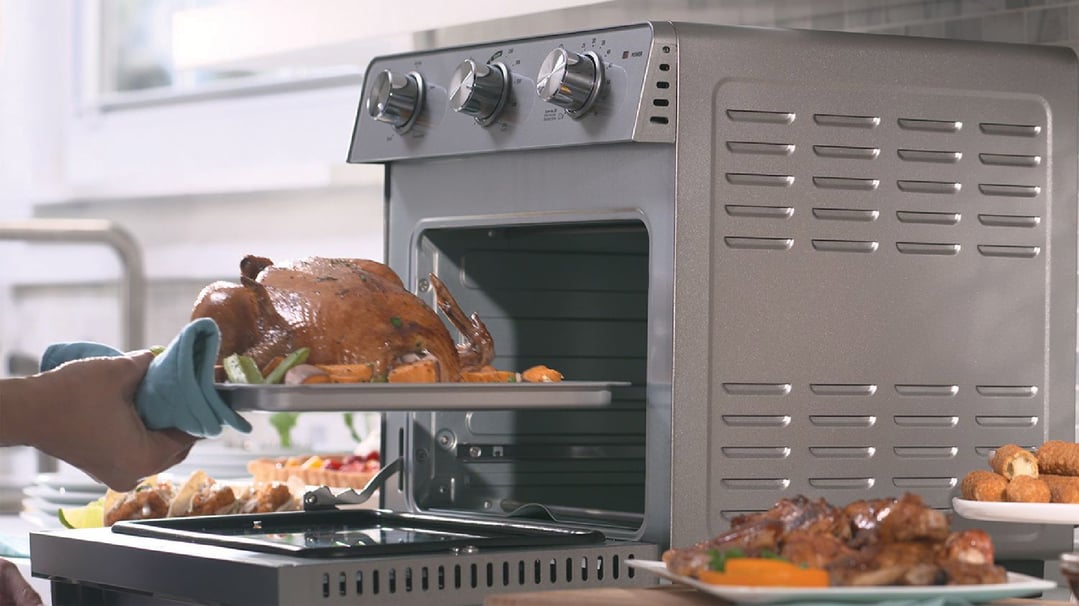 Hands in oven mitts placing a roasted chicken into a Multi Function Oven + Air Fryer
