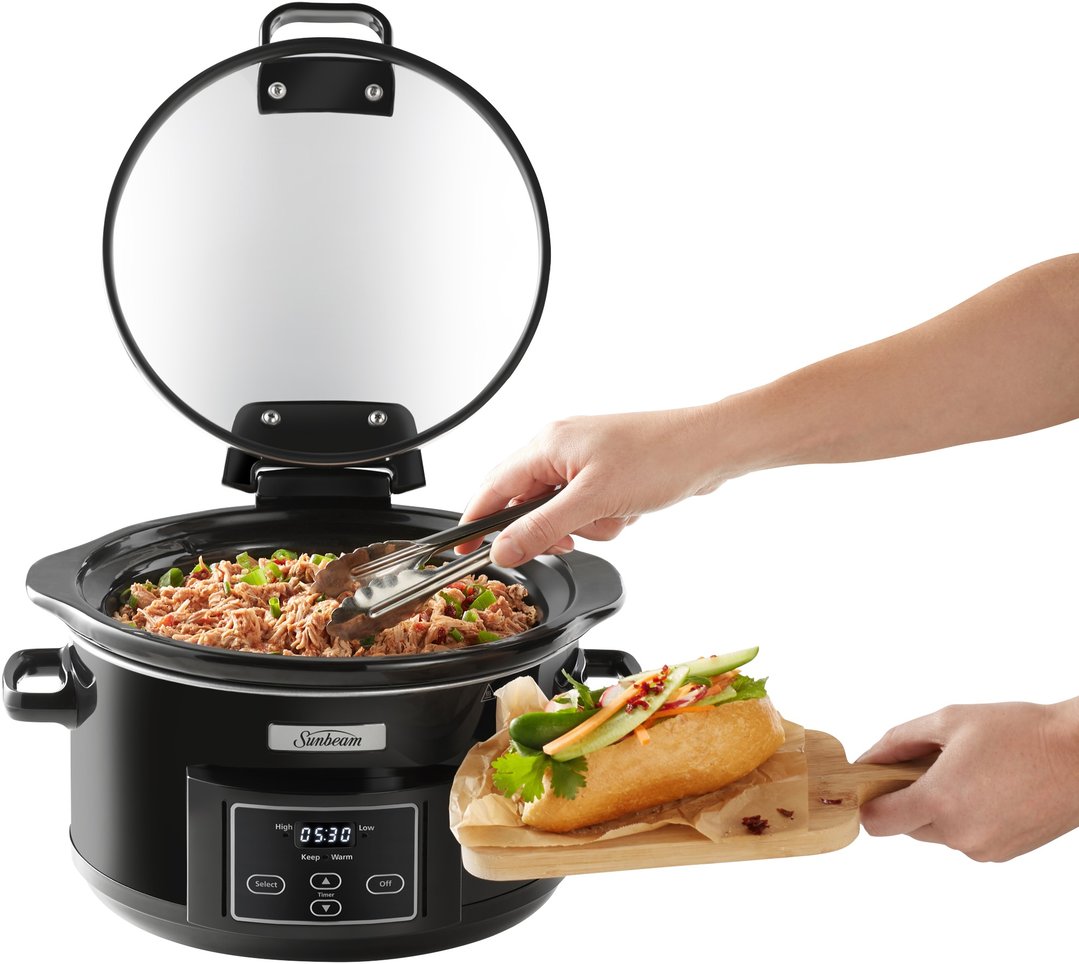 Hands using tongs to serve food from a black slow cooker onto a sandwich